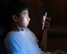 Nastolatek w ciemnym pokoju, wpatrujący się w świecący ekran smartfona