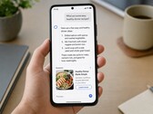Dłoń trzymająca smartfon, na którym wyświetla się odpowiedź generowana przez sztuczną inteligencję, a poniżej znajduje się reklama sponsorowana