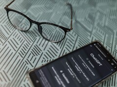 Smartfon z uruchomioną aplikacją ChatGPT obok pary okularów na wzorzystej powierzchni