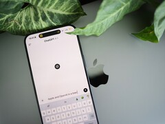 Smartfon z uruchomioną aplikacją ChatGPT, leżący na laptopie obok liści rośliny
