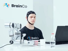 Użytkownik technologii sterowania umysłem firmy BrainCo, który za pomocą samych myśli w sposób automatyczny chwyta jabłko.