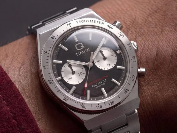 Zegarek Timex Q Timex Continental Chronograph TW2Y93200 na nadgarstku, wyposażony w czarną tarczę o promienistym wzorze przypominającym płytę CD, dwie srebrne tarcze pomocnicze, pierścień z tachymetrem, świecące znaczniki oraz zintegrowaną bransoletę ze stali nierdzewnej.