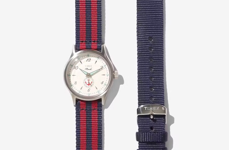 Model Noah x Timex MK1 Anchor z czerwono-czarnym paskiem z tkaniny przedstawiony obok paska w jednolitym niebieskim kolorze.