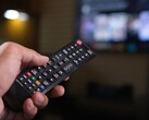 Dłoń trzymająca pilota z rozmytym telewizorem w tle