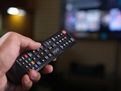 Dłoń trzymająca pilota z rozmytym telewizorem w tle