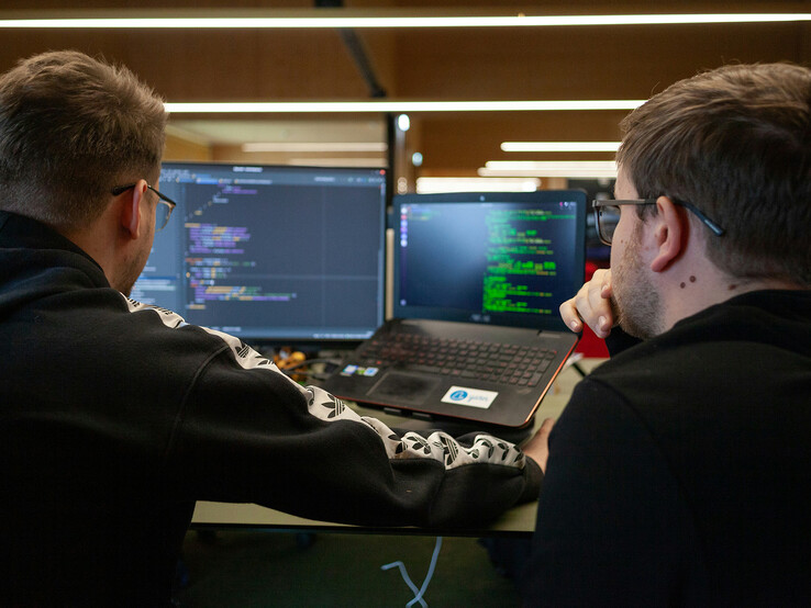 Naukowcy analizujący kod na dwóch monitorach (źródło obrazu: Flipsnack / Unsplash)
