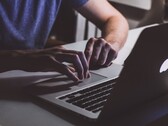Ręce piszące na klawiaturze MacBooka w słabym świetle, świecące logo Apple