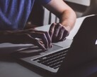 Ręce piszące na klawiaturze MacBooka w słabym świetle, świecące logo Apple