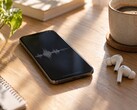 Smartfon wyświetlający przebieg fali dźwiękowej obok bezprzewodowych słuchawek dousznych i filiżanki kawy na drewnianym biurku