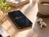 Smartfon wyświetlający przebieg fali dźwiękowej obok bezprzewodowych słuchawek dousznych i filiżanki kawy na drewnianym biurku