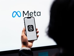 Dłoń trzyma smartfon przed dużym logo Meta