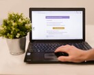 Laptop na biurku z otwartą skrzynką odbiorczą poczty elektronicznej, obok którego stoi roślina doniczkowa.