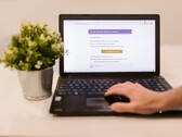 Laptop na biurku z otwartą skrzynką odbiorczą poczty elektronicznej, obok którego stoi roślina doniczkowa.
