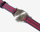 Widok z tyłu zegarka Noah x Timex MK1 Anchor, ukazujący grawerowany dekiel z nierdzewnej stali oraz pasek z tkaniny w kolorach granatowym i czerwonym.