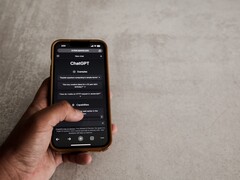 Dłoń trzymająca smartfon z interfejsem ChatGPT na ekranie nad szarą kamienną powierzchnią