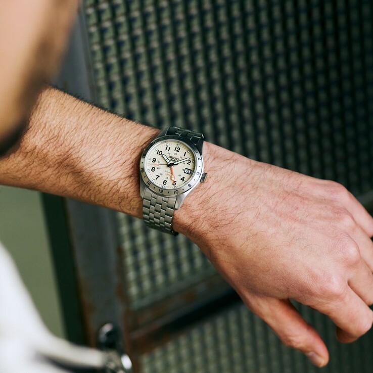 Widok z przodu zegarka Seiko 5 Sports Field GMT HDB002 z kremową tarczą, pomarańczową wskazówką GMT, nieruchomą 24-godzinną ramką oraz bransoletą ze stali nierdzewnej.