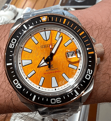 Zbliżenie na model Seiko Prospex HBB005K1 przedstawiające teksturowaną bursztynową tarczę, powiększone świecące znaczniki godzinowe, szerokie wskazówki, okienko datownika oraz czarną obwódkę nurkową z pomarańczowymi oznaczeniami.