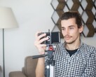 Młody mężczyzna filmuje siebie w domu za pomocą smartfona zamontowanego na statywie