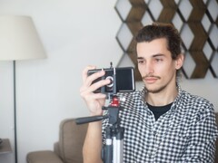 Młody mężczyzna filmuje siebie w domu za pomocą smartfona zamontowanego na statywie