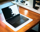 Otwarty, matowo-czarny laptop gamingowy Razer Blade 16 stojący na białej podkładce biurkowej, umieszczonej na ciepłym drewnianym stole, z wyświetlaną na ekranie wyrazistą czarno-białą tapetą.