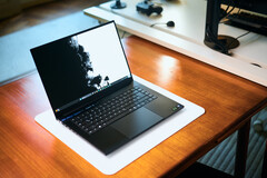 Otwarty, matowo-czarny laptop gamingowy Razer Blade 16 stojący na białej podkładce biurkowej, umieszczonej na ciepłym drewnianym stole, z wyświetlaną na ekranie wyrazistą czarno-białą tapetą.