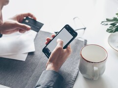 Osoba stukająca w ekran smartfona, trzymając w drugiej ręce kartę bankową
