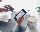 Osoba stukająca w ekran smartfona, trzymając w drugiej ręce kartę bankową