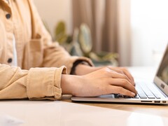 Ręce piszące na klawiaturze otwartego laptopa na jasnym biurku