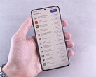 Dłoń trzyma smartfon, na którego ekranie wyświetla się lista aktualizacji.