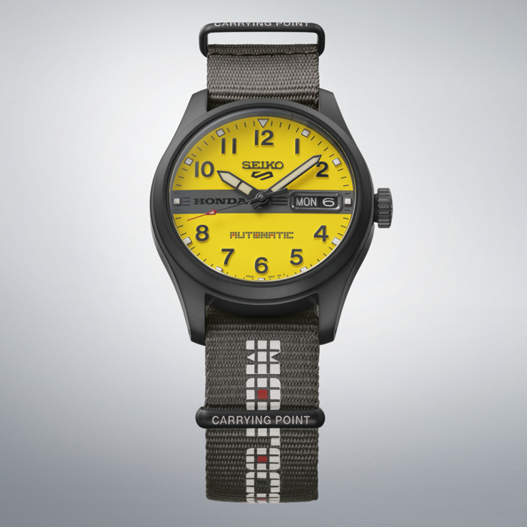 Widok z przodu zegarka Seiko 5 Sports Field x Honda Motocompo Limited Edition z żółtą tarczą, czarnym logo Hondy pośrodku oraz szarym nylonowym paskiem.