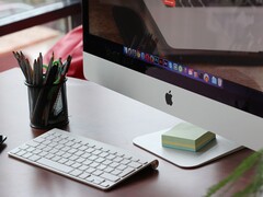 Komputer iMac na biurku z widocznym na ekranie paskiem dokowania systemu macOS oraz klawiaturą Apple przed nim