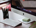 Komputer iMac na biurku z widocznym na ekranie paskiem dokowania systemu macOS oraz klawiaturą Apple przed nim