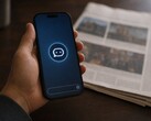 Ręka trzyma smartfon z ikoną chatbota, a obok niego leży wydrukowana gazeta.