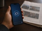 Ręka trzyma smartfon z ikoną chatbota, a obok niego leży wydrukowana gazeta.