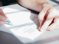 Ręka podpisuje dokument niebieskim długopisem