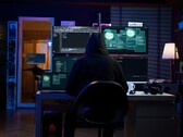 Zakapturzona postać przy wieloekranowej konfiguracji przeprowadzającej cyberatak. 