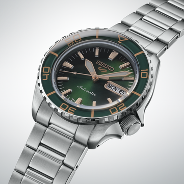Zbliżenie na Seiko 5 Sports SKX HDB005, ukazujące ciemnozieloną tarczę, wskazówki i nakładane indeksy w kolorze różowego złota oraz dopasowaną zieloną lunetę z oznaczeniami w kolorze złota.