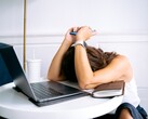 Kobieta spoglądająca w dół na swój smartfon, obok niej znajduje się laptop