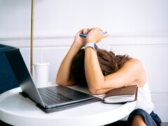 Kobieta spoglądająca w dół na swój smartfon, obok niej znajduje się laptop
