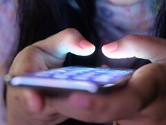 Dwie dłonie trzymają smartfon ze świecącym ekranem w przyćmionym świetle
