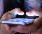 Dwie dłonie trzymają smartfon ze świecącym ekranem w przyćmionym świetle