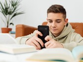 Nastolatek w bluzie z kapturem piszący na smartfonie, mając przed sobą otwarte podręczniki szkolne