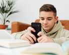 Nastolatek w bluzie z kapturem piszący na smartfonie, mając przed sobą otwarte podręczniki szkolne