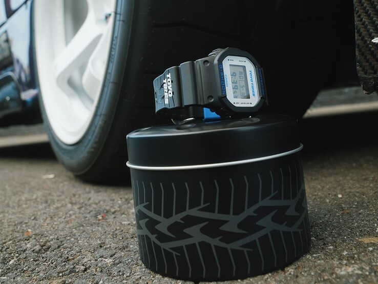 Zegarek Casio G-Shock DW5600TT25-1 x Toyo Tires wyeksponowany na metalowej puszce o motywie opony, obok koła samochodowego.