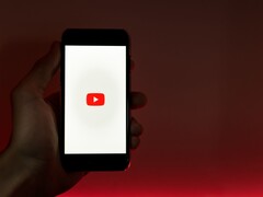Dłoń trzymająca smartfon z podświetlonym na wyświetlaczu logo YouTube na czerwonym tle