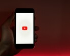 Dłoń trzymająca smartfon z podświetlonym na wyświetlaczu logo YouTube na czerwonym tle