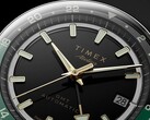 Zbliżenie na czarną tarczę modelu Timex Atelier GMT Première M1a ze wskazówkami w kolorze złotym, świecącymi indeksami godzinowymi, okienkiem datownika oraz czarno-zielonym pierścieniem GMT z podziałką 24-godzinną.