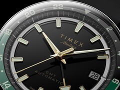 Zbliżenie na czarną tarczę modelu Timex Atelier GMT Première M1a ze wskazówkami w kolorze złotym, świecącymi indeksami godzinowymi, okienkiem datownika oraz czarno-zielonym pierścieniem GMT z podziałką 24-godzinną.