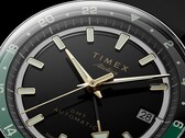 Zbliżenie na czarną tarczę modelu Timex Atelier GMT Première M1a ze wskazówkami w kolorze złotym, świecącymi indeksami godzinowymi, okienkiem datownika oraz czarno-zielonym pierścieniem GMT z podziałką 24-godzinną.