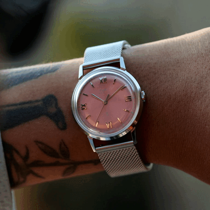 Osoba nosząca zegarek Timex x Todd Snyder Marlin Mesh z tarczą w kolorze łososiowym z efektem promieniowania słonecznego oraz bransoletą z siateczki.